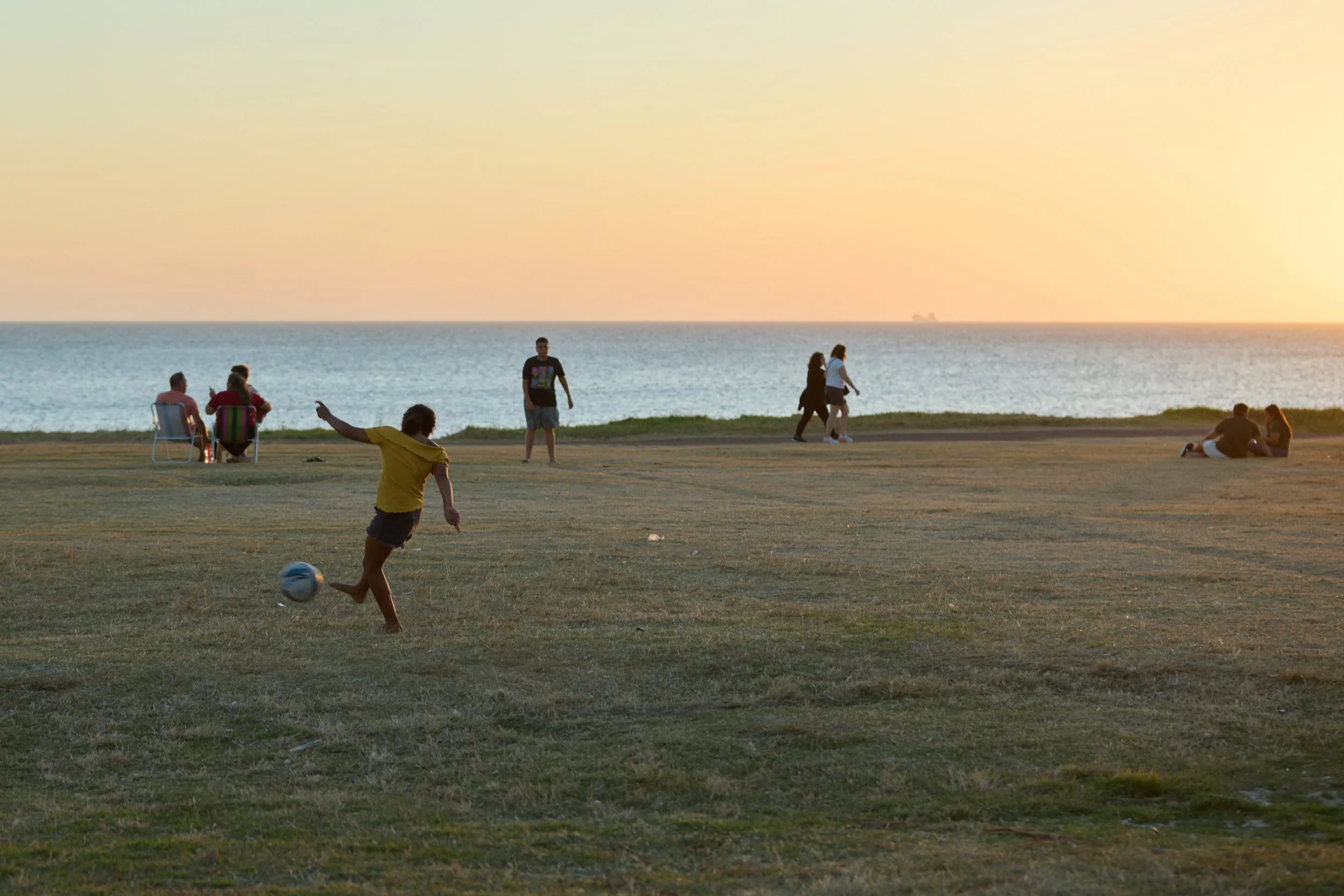 Un partido de fútbol en el pasto de la Rambla de Punta Carretas, al atardecer