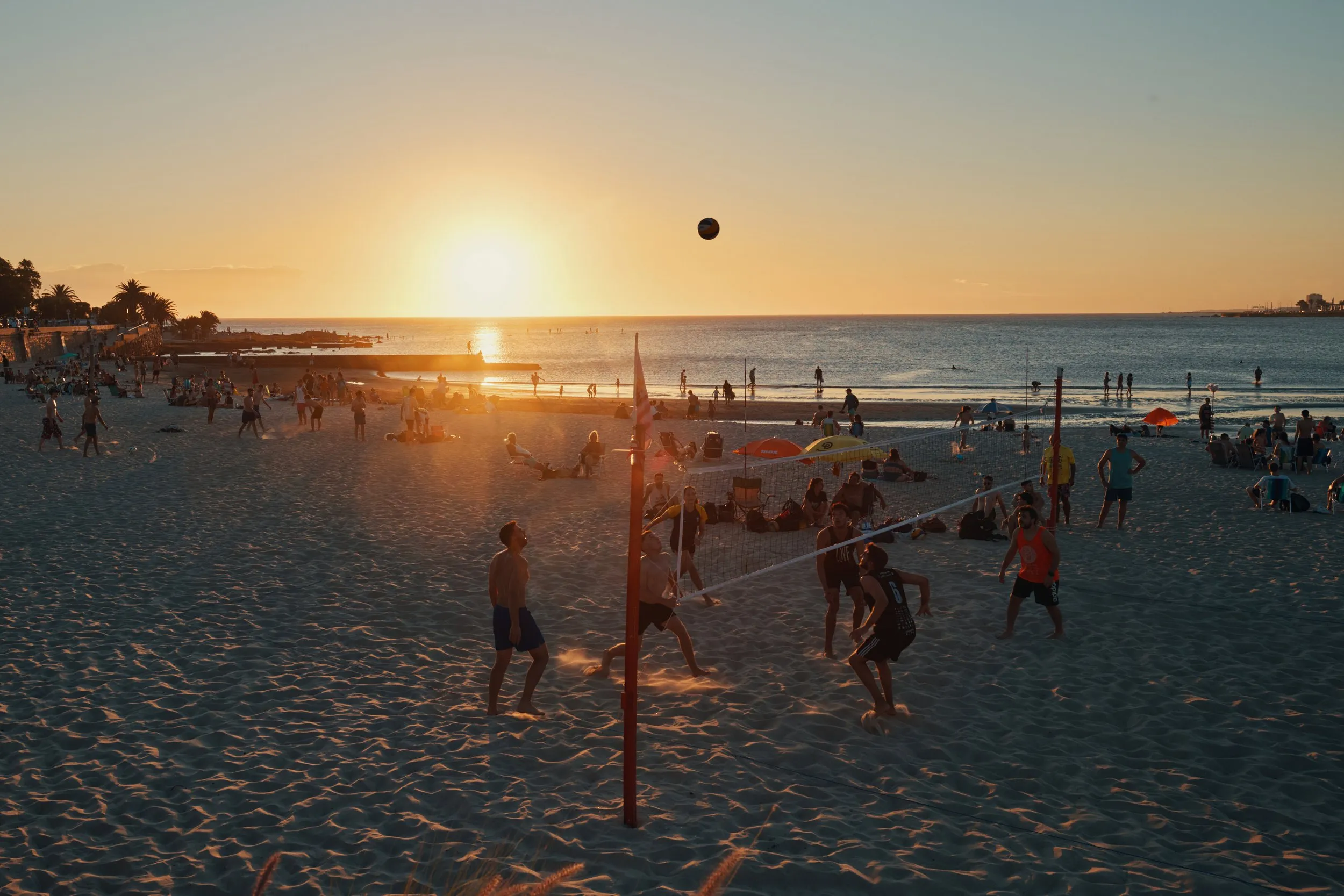 Un partido de vóley en la playa al atardecer, con el sol bajando sobre el agua