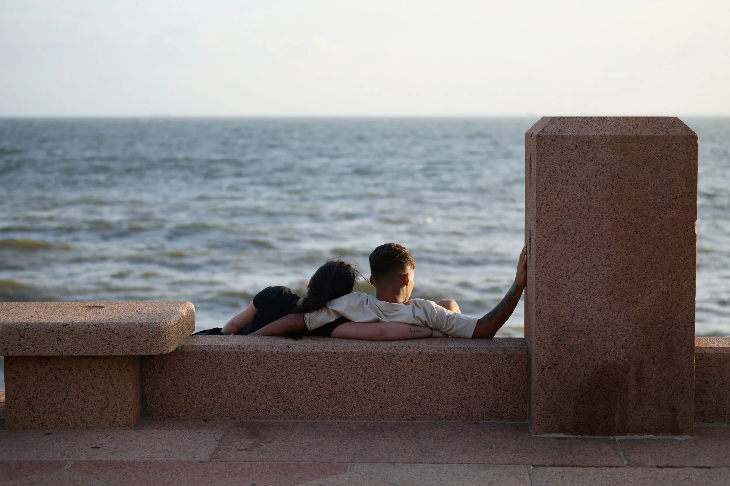 Una pareja sentada en el parapeto de la rambla, mirando el río