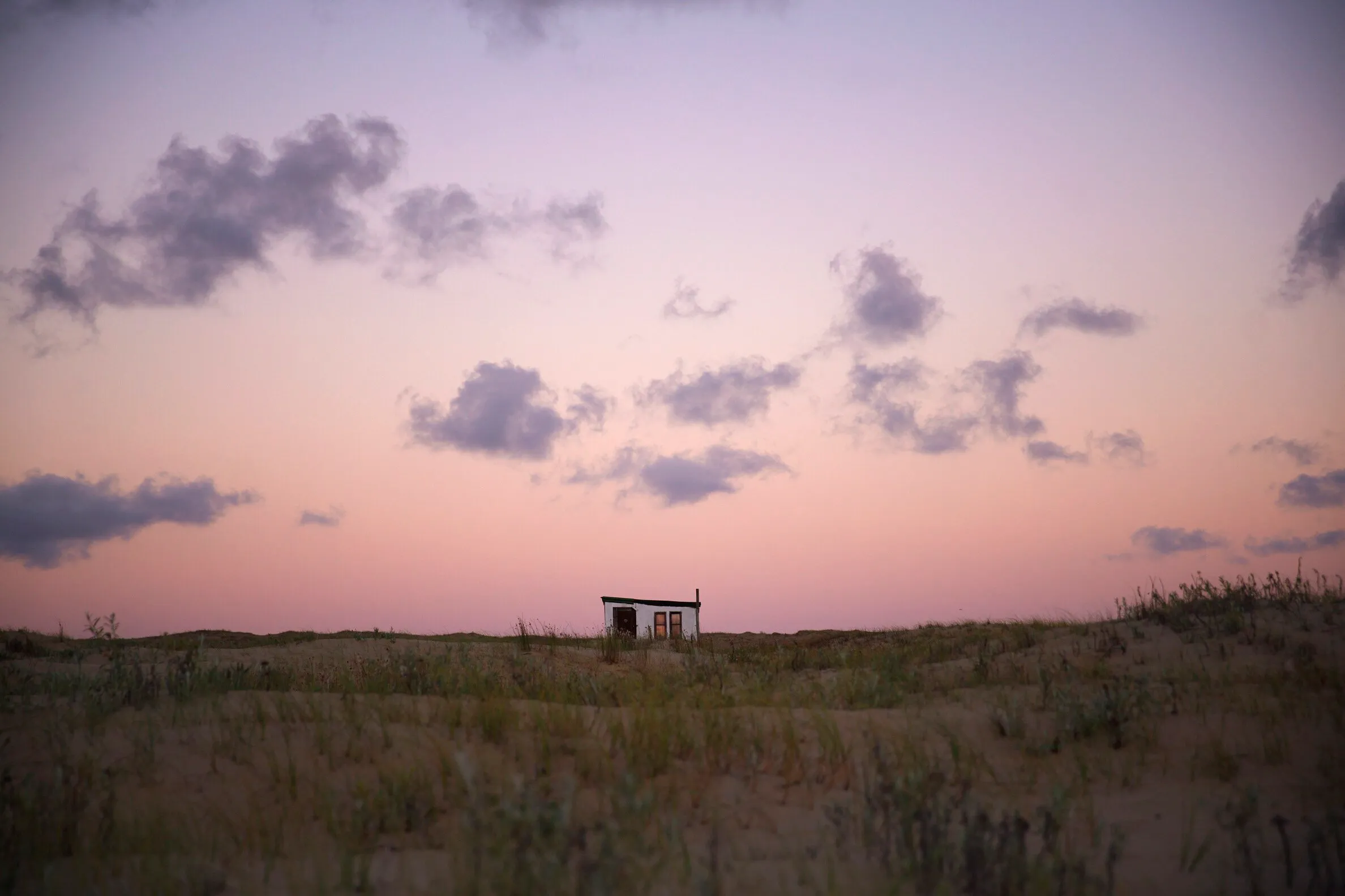 Un rancho bajo entre los pastizales de Cabo Polonio, bajo un cielo lila
