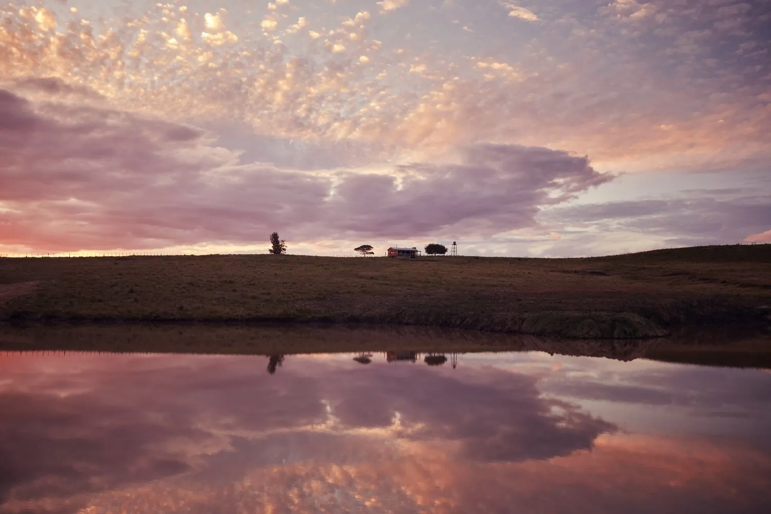 Un amanecer rosado reflejado en el agua, con una casa en la loma, en Garzón