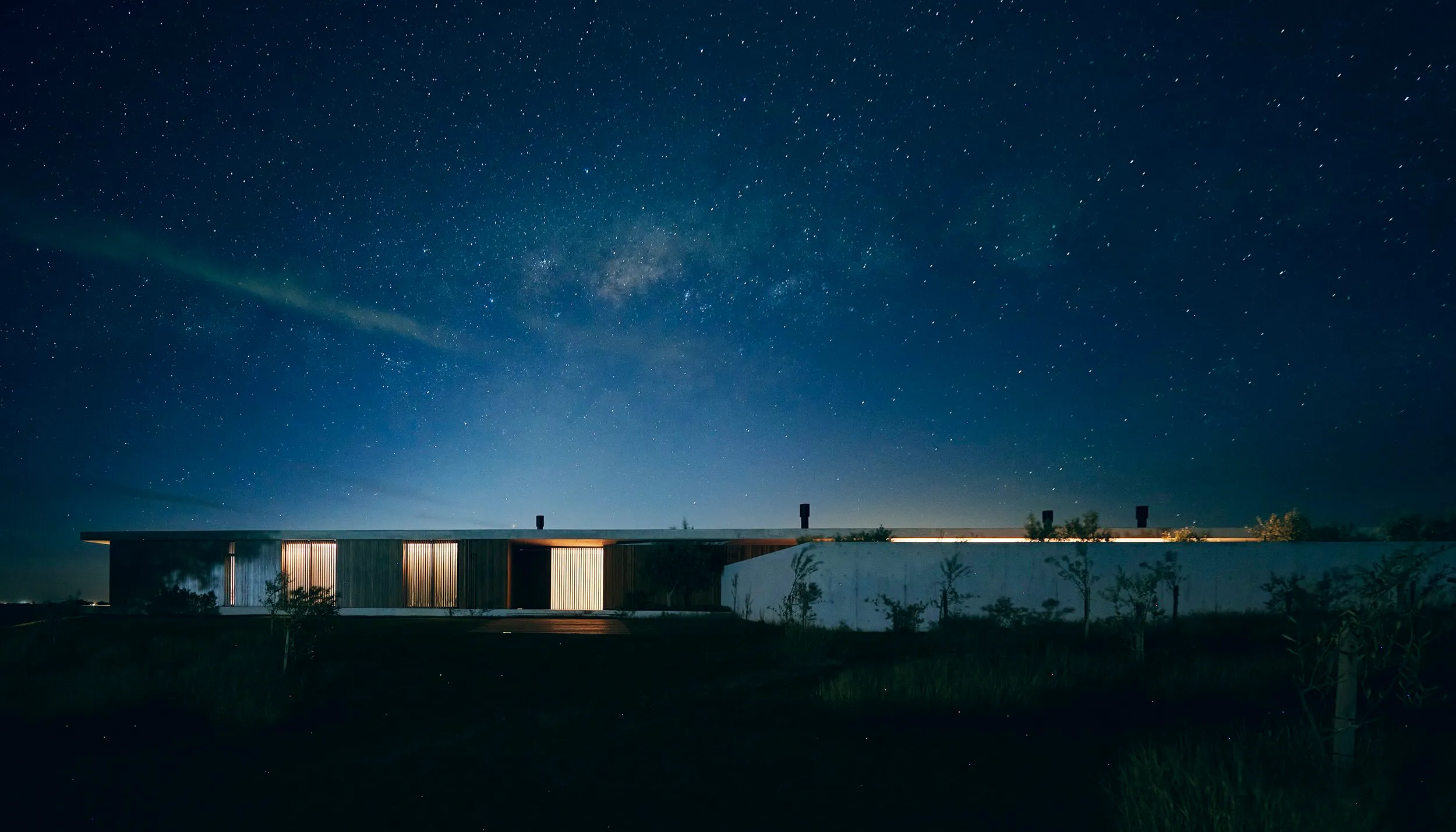 Edificio moderno y plano en un entorno oscuro con un cielo despejado lleno de estrellas y la vía láctea visible.