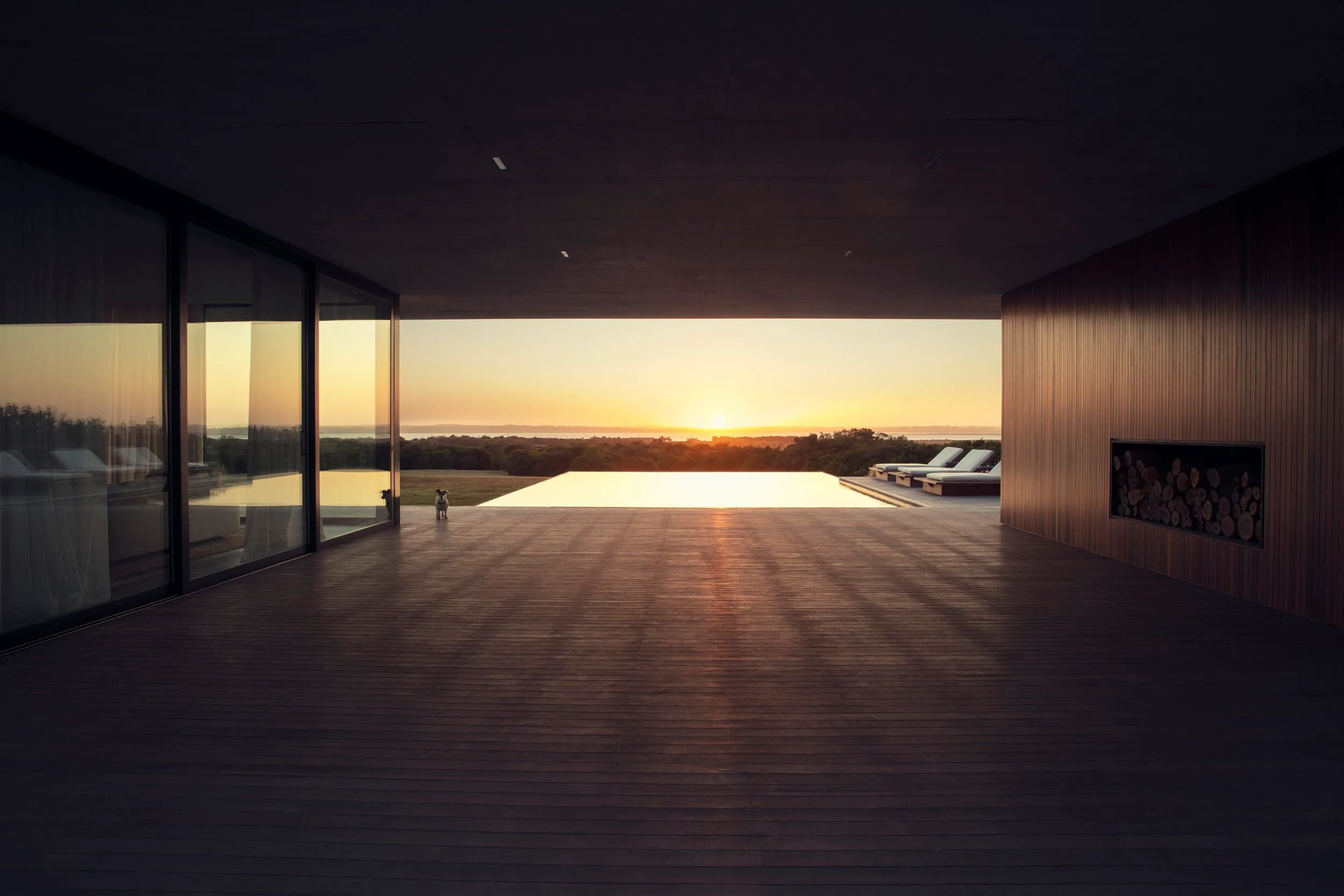 Terraza moderna con vistas al atardecer, sillones y chimenea de leña integrada.