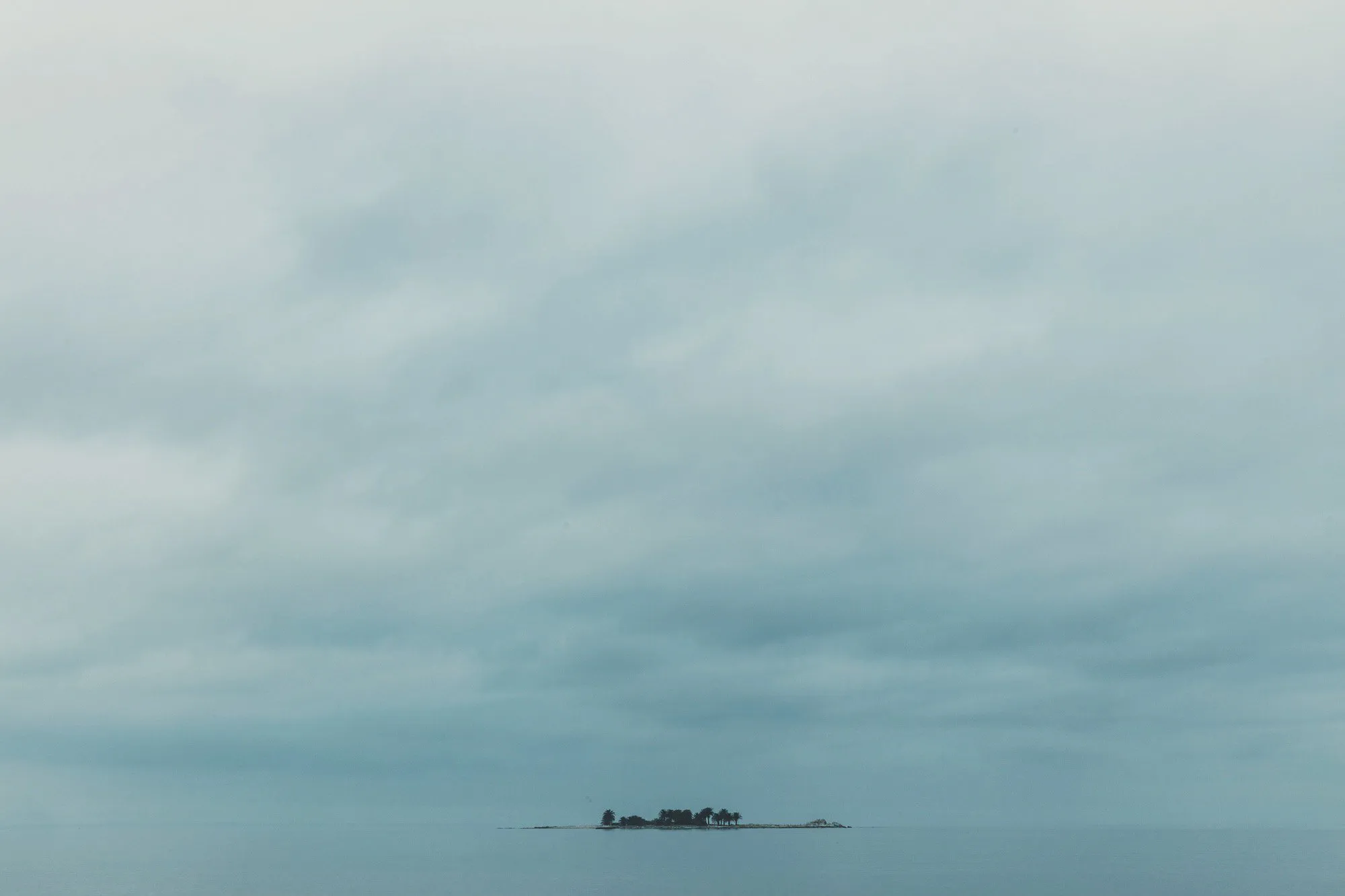 Una isla diminuta con unos árboles, sola en el mar bajo un cielo gris