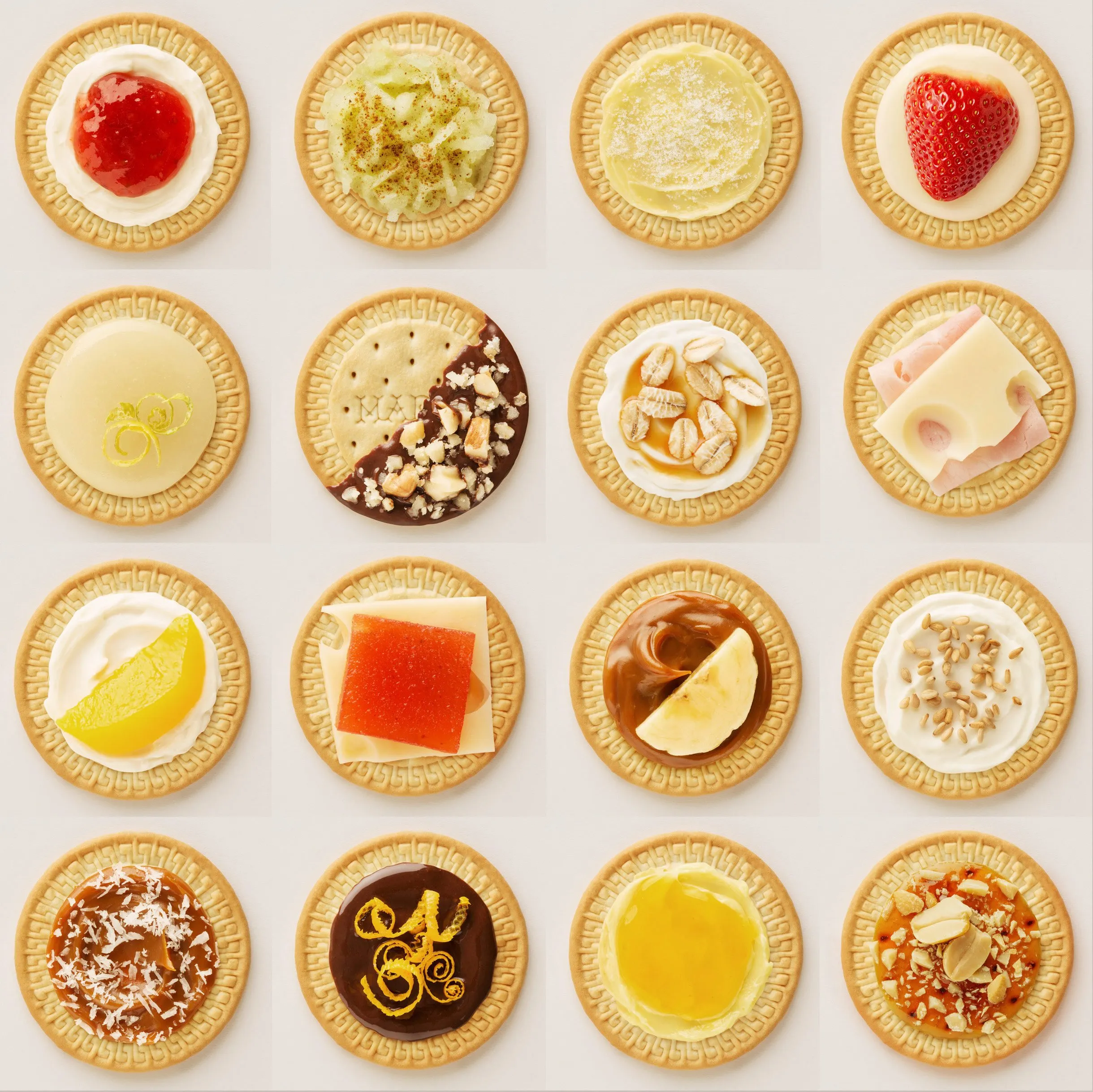 Un arreglo de quince galletas decoradas con diferentes coberturas y toppings, incluyendo mermelada, crema, frutas y chocolates.