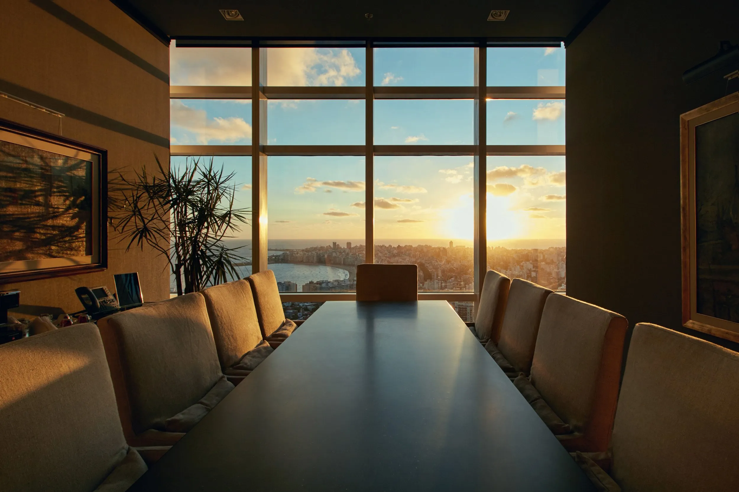 Sala de reuniones con gran ventana panorámica que muestra un atardecer sobre la ciudad