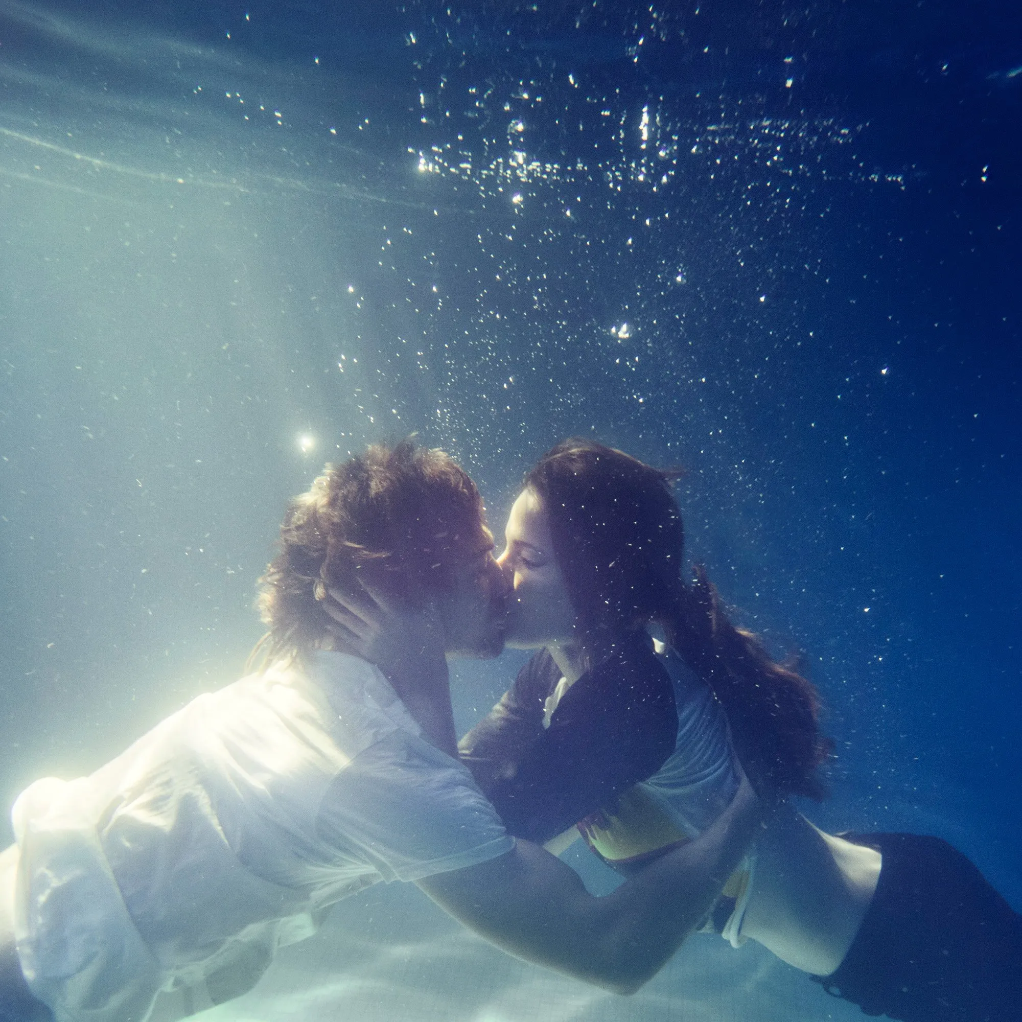 Una pareja besándose bajo el agua, rodeados de burbujas y luz