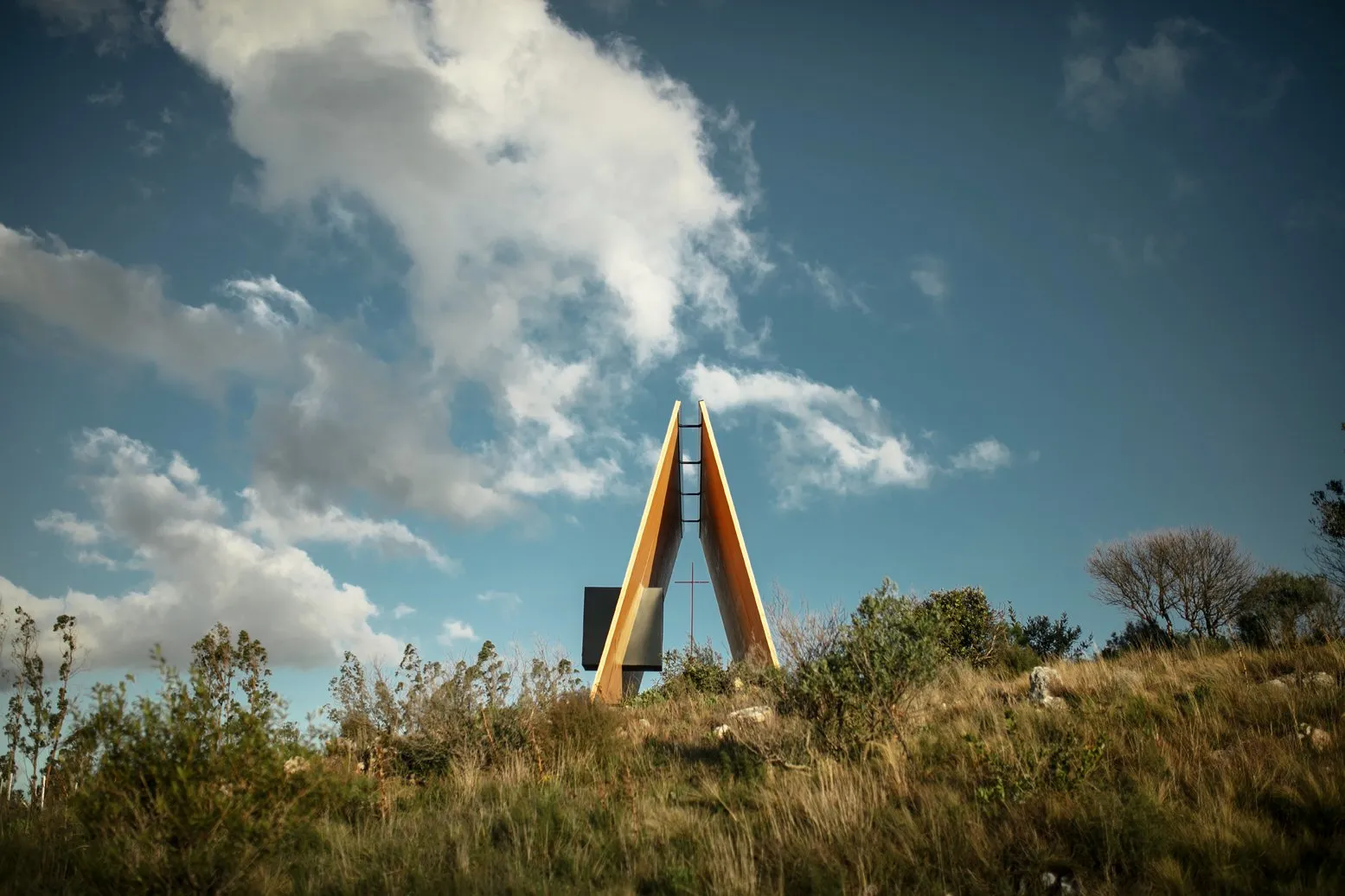 Estructura moderna en una colina con árboles y cielo nublado de fondo.