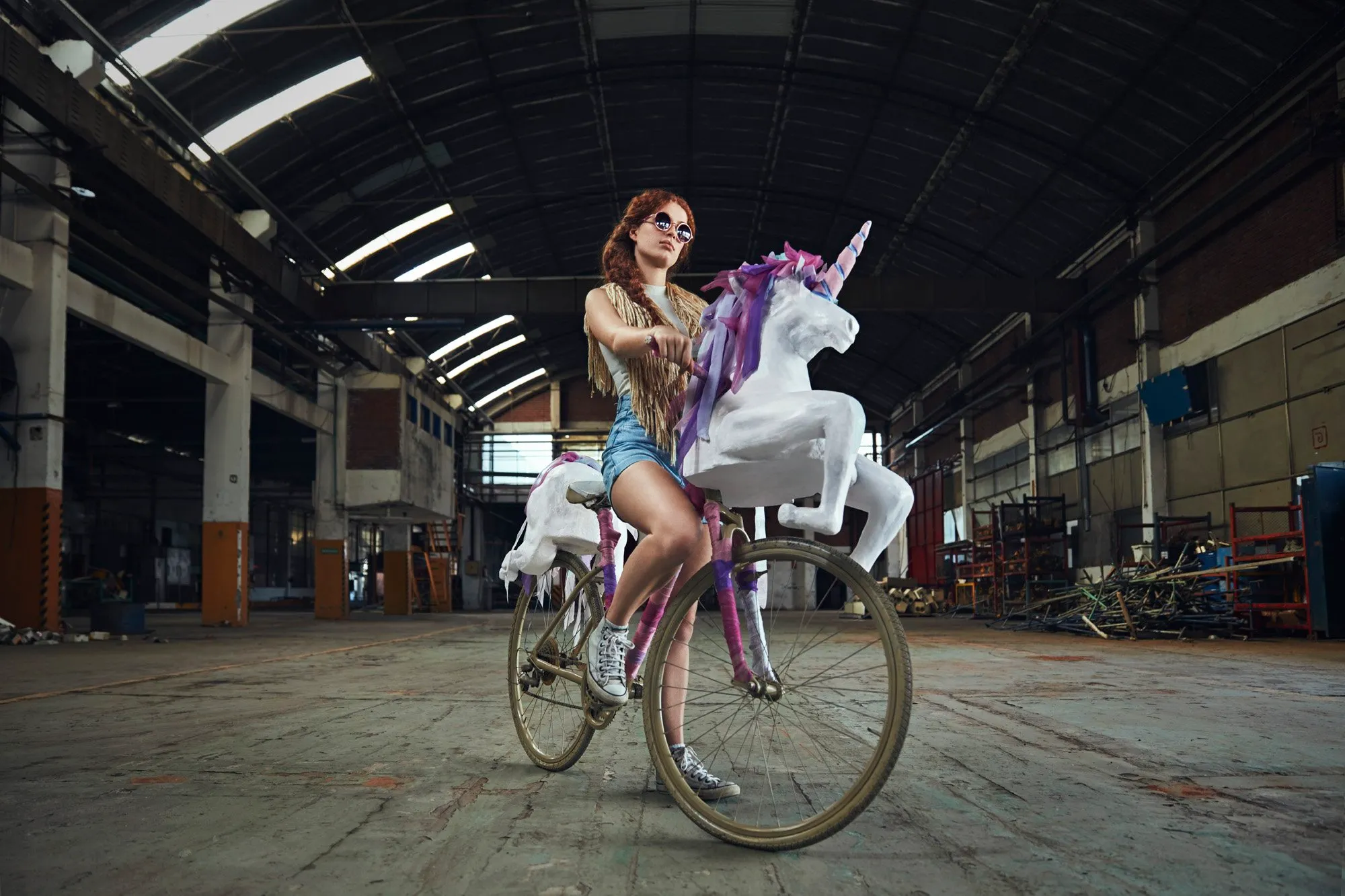 Una mujer montando una bicicleta decorada con un unicornio, en un espacio industrial