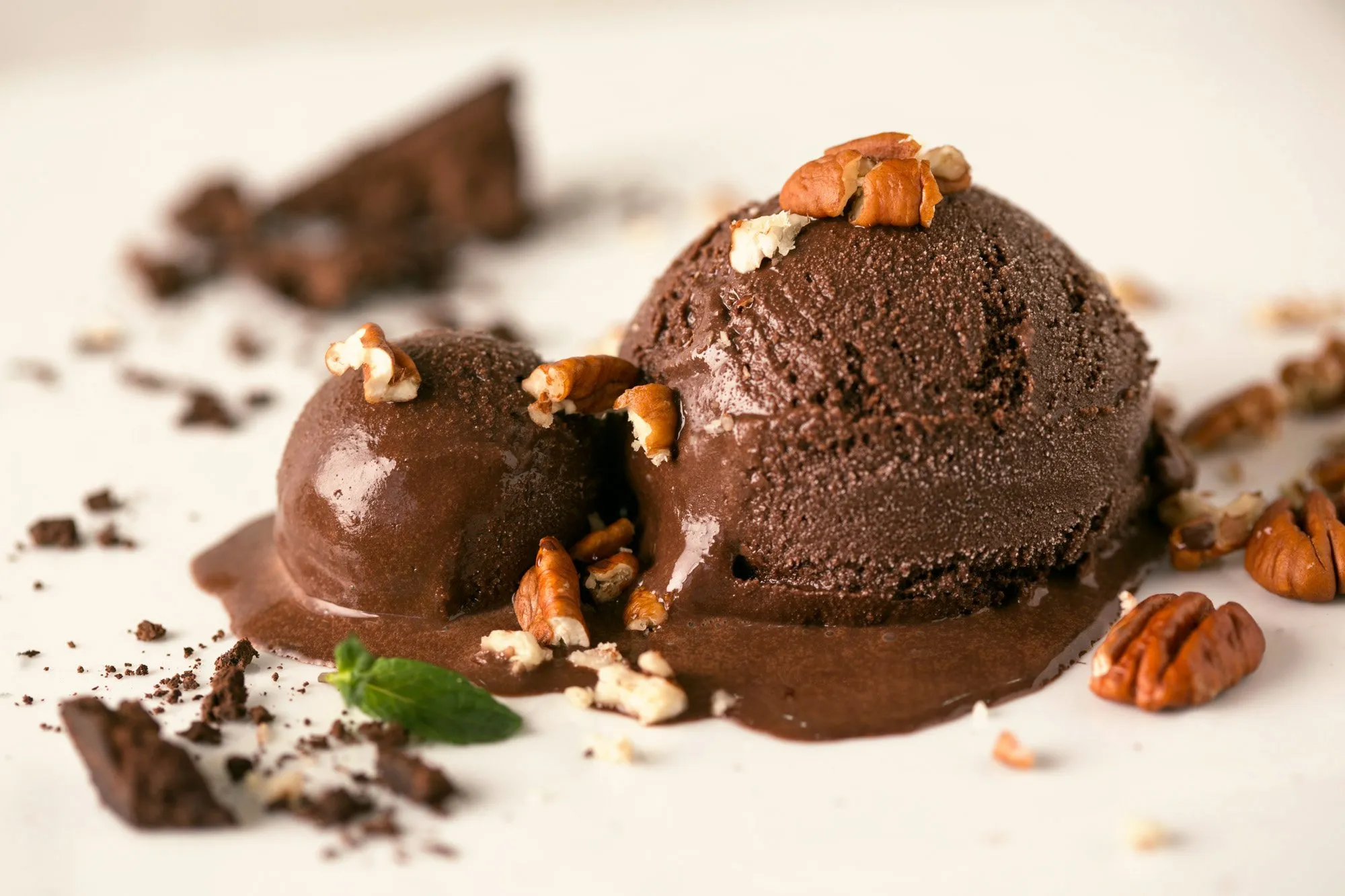 Dos bolas de helado de chocolate con nueces picadas y chocolate rallado decorativas en un plato blanco.