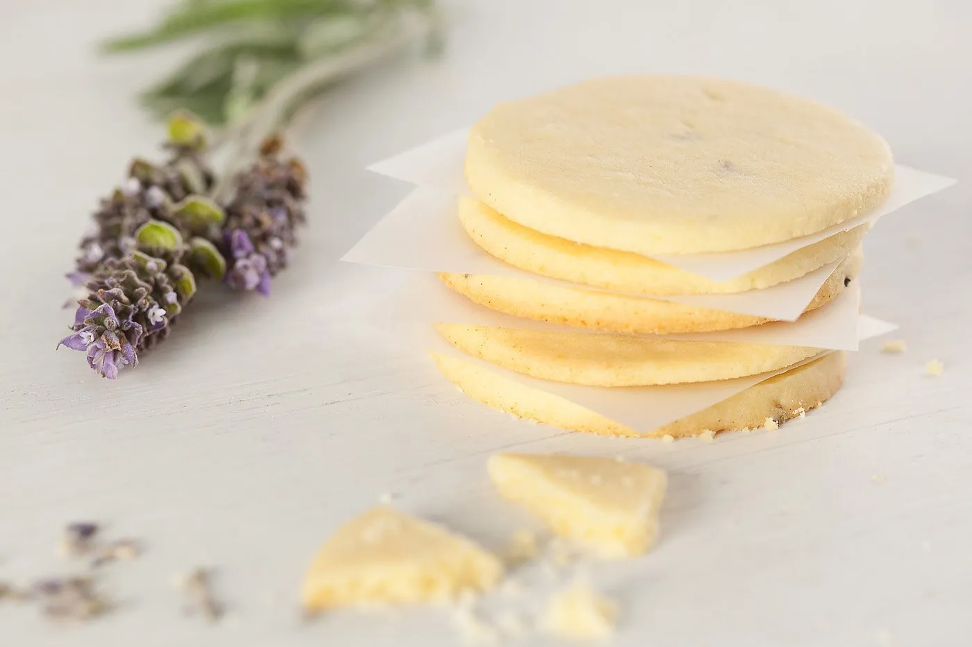 Cuatro galletas sabor queso con papel en medio, junto a flores de lavanda y pedazos de queso.