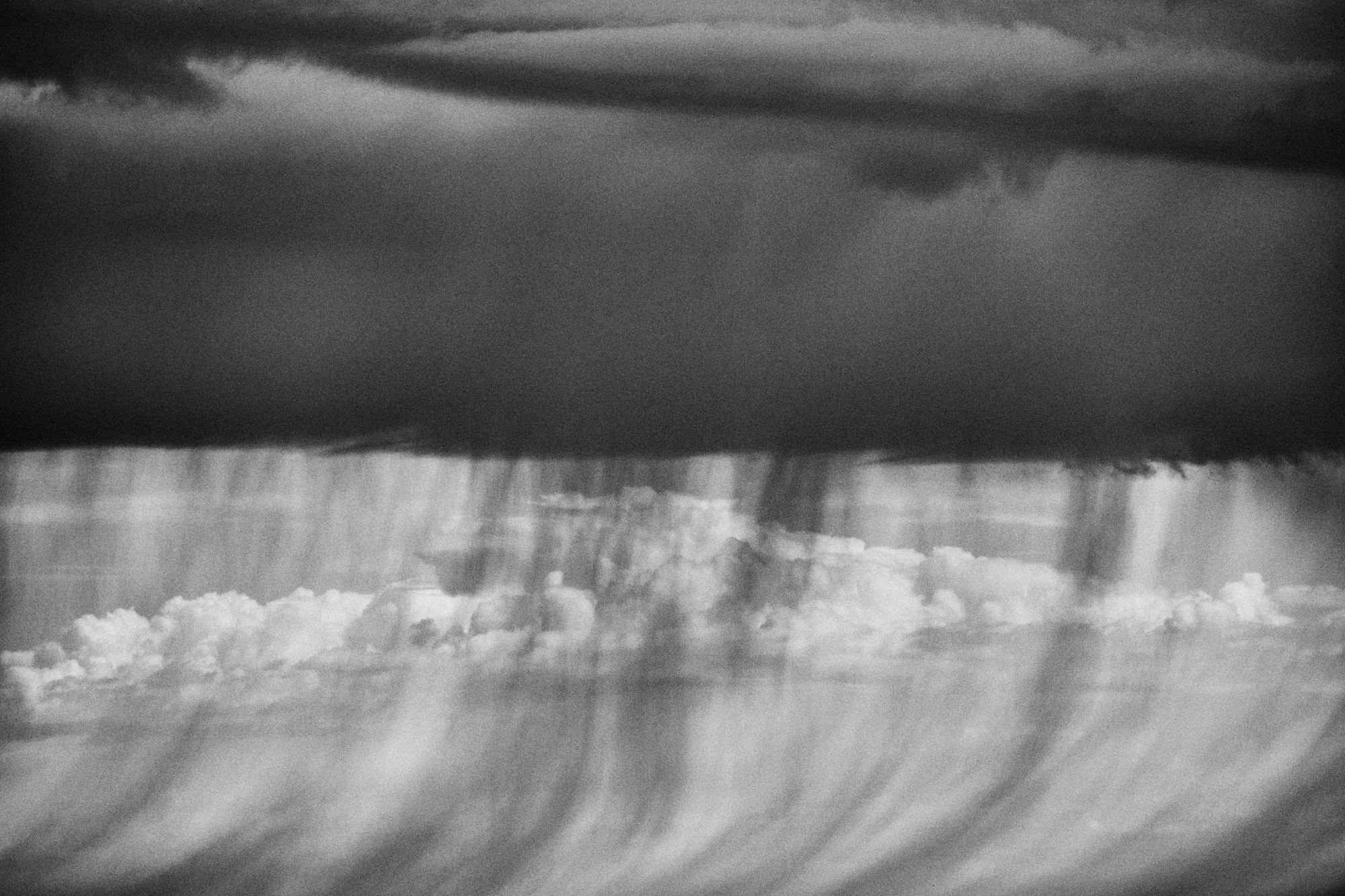 Cortinas de lluvia cayendo desde una nube alargada, en blanco y negro