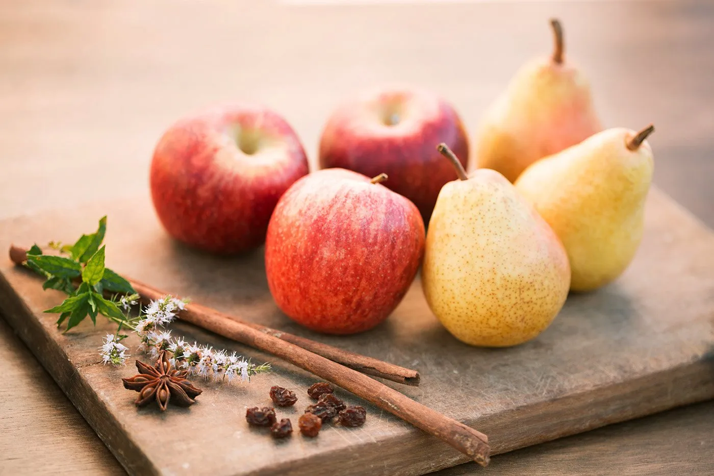 Manzanas y peras sobre tabla de madera con especias y flores.