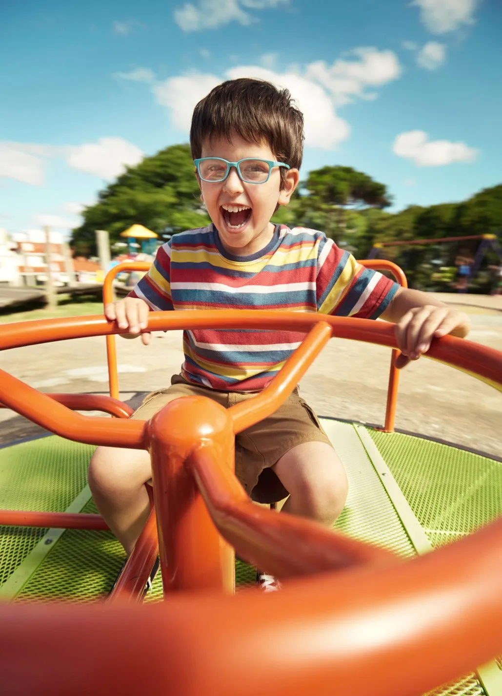 Niño sonriendo y disfrutando mientras gira en un caballito de parque con fondo de cielo azul y árboles.