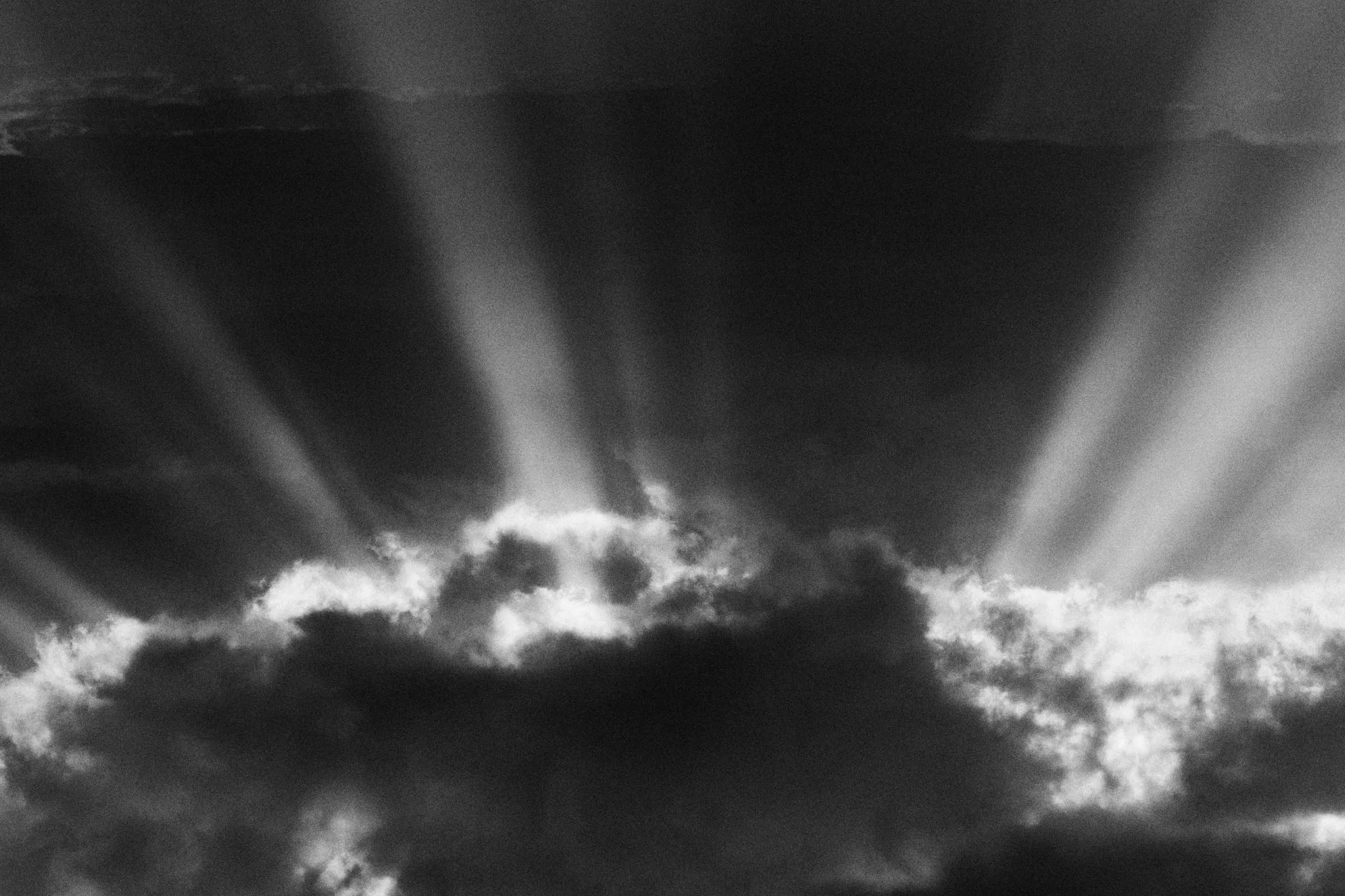 Rayos de sol abriéndose por encima de una nube oscura, en blanco y negro