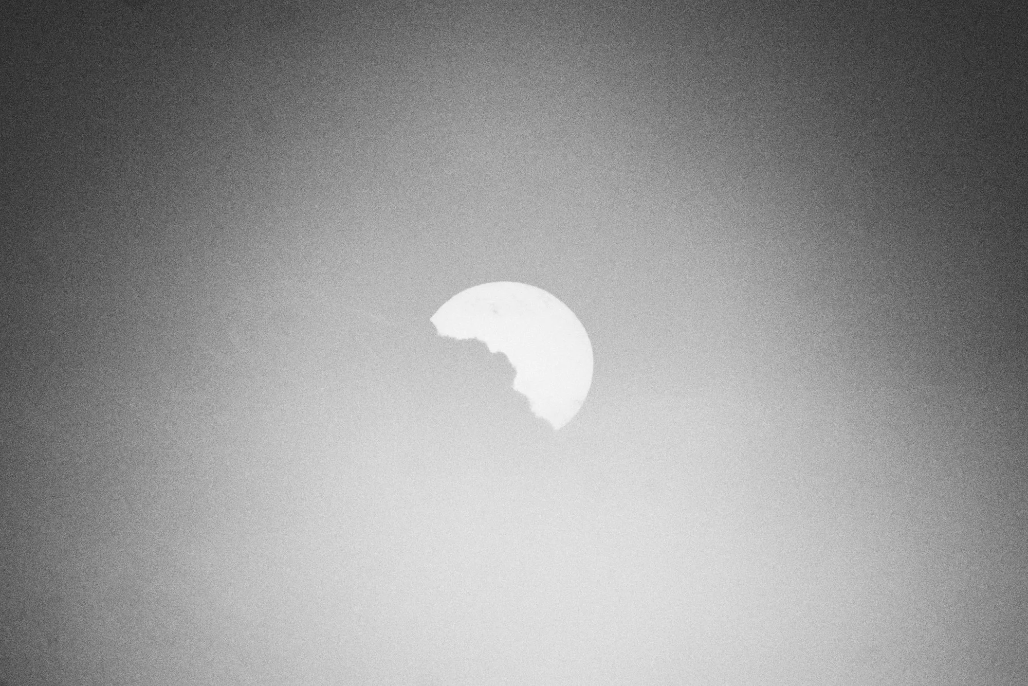 El sol asomando detrás de una nube, en un cielo encendido, en blanco y negro