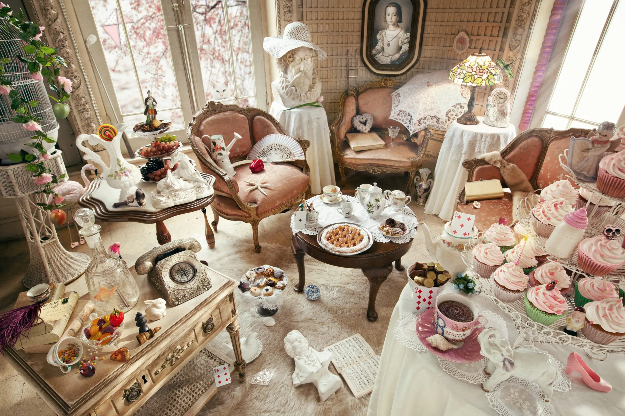 Una sala decorada en estilo vintage con muebles y objetos de porcelana, tazas de té, pastelitos, cupcakes con glaseado rosa, un telón de fondo con ventanas grandes y un ambiente coqueto y ecléctico.